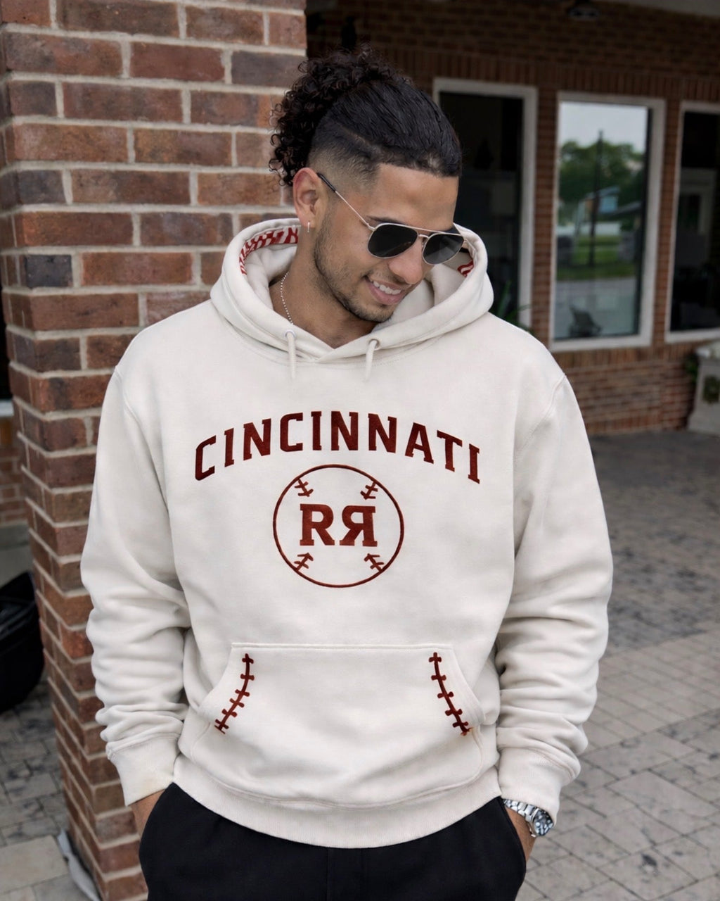 Man wearing a white hoodie with 'Cincinnati RR' print, standing in front of a brick building.