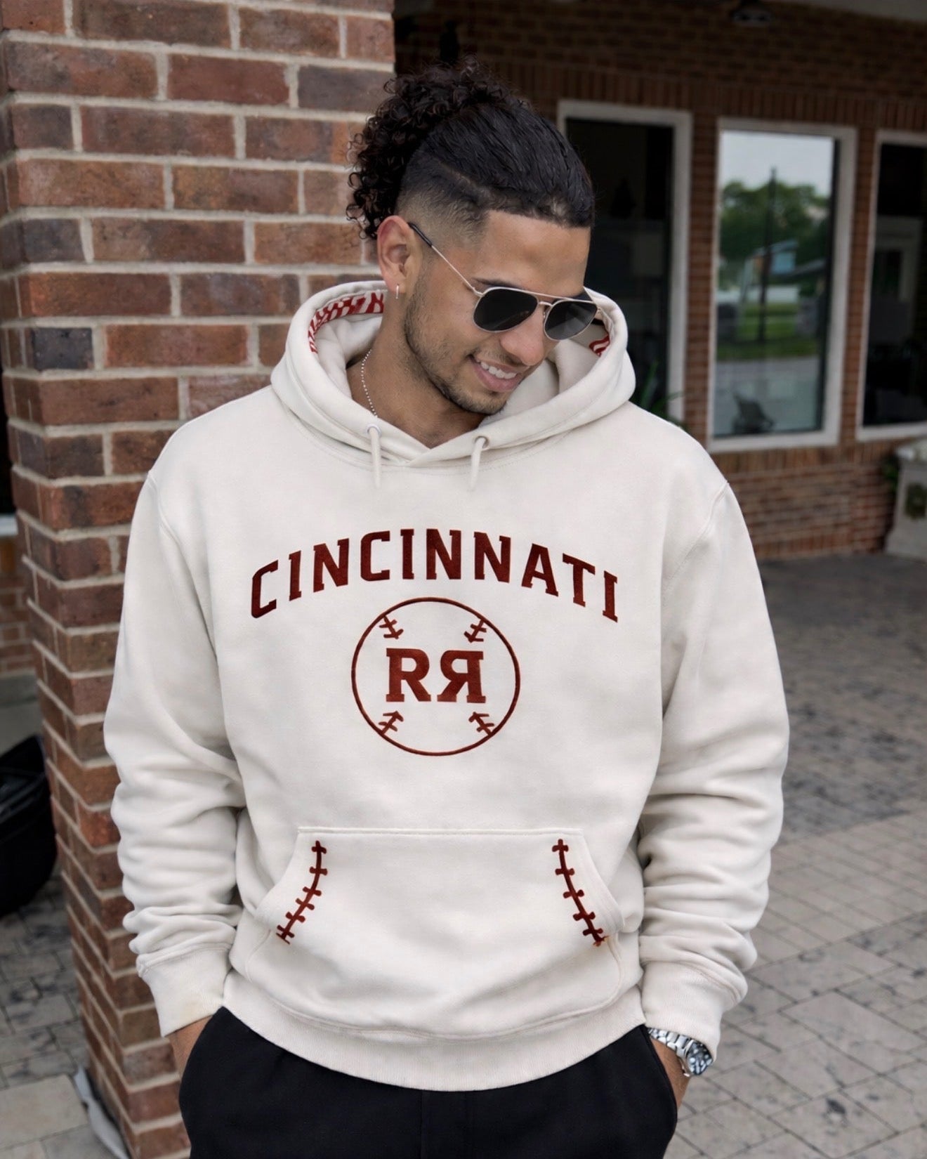 Man wearing a white hoodie with 'Cincinnati RR' print, standing in front of a brick building.