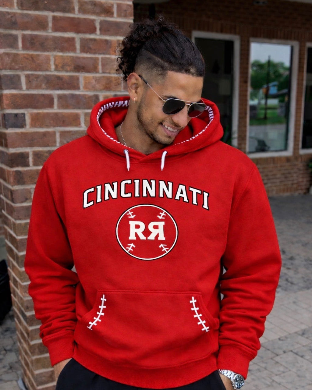 Person wearing a red 'Cincinnati' hoodie with a logo, standing against a brick wall.