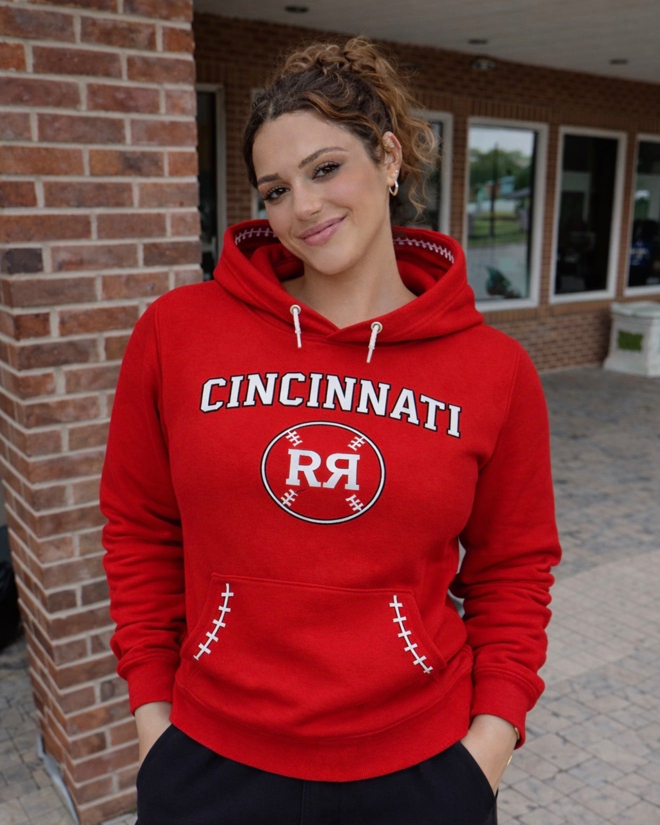 Person wearing a red 'Cincinnati' hoodie with a logo, standing in front of a brick building.